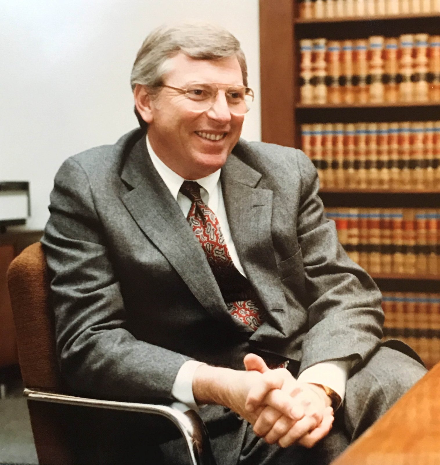 Mark White in a gray suit seated in a law library, smiling.